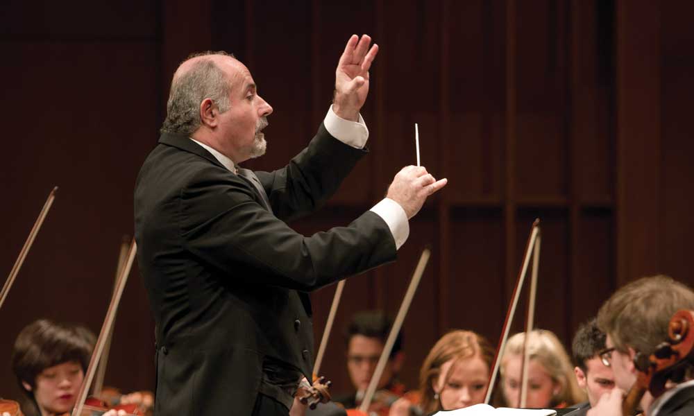 A conductor in front of string players conducting.