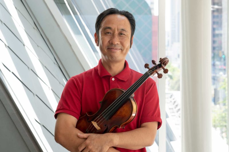 Chan Ho Yun holding a violin and smiling in front of a window.
